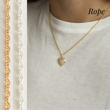 A gold heart locket with a gold rope chain on a model wearing a white top.