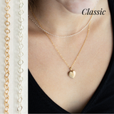 A gold heart locket with a gold chain layered with a silver chain. The model is wearing a black top. 
