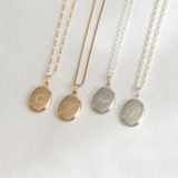 A collection of oval lockets in gold and silver colors, each with a different letter engraved on it. They are displayed along with their respective chains.