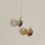 Two lockets, one gold and one silver, on a flat surface. Both are opened to display the engraving and photos inside.