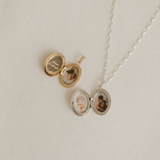 A gold and silver locket on a white surface open to show the inside engraving and photos.