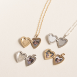 Multiple heart lockets, gold colored and silver colored, on a flat white surface, open to show the engravings and photos on the inside.