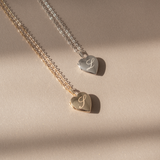Two heart lockets on a chain, one gold-colored and one silver-colored, lying on a flat surface with a shadow cast over them.